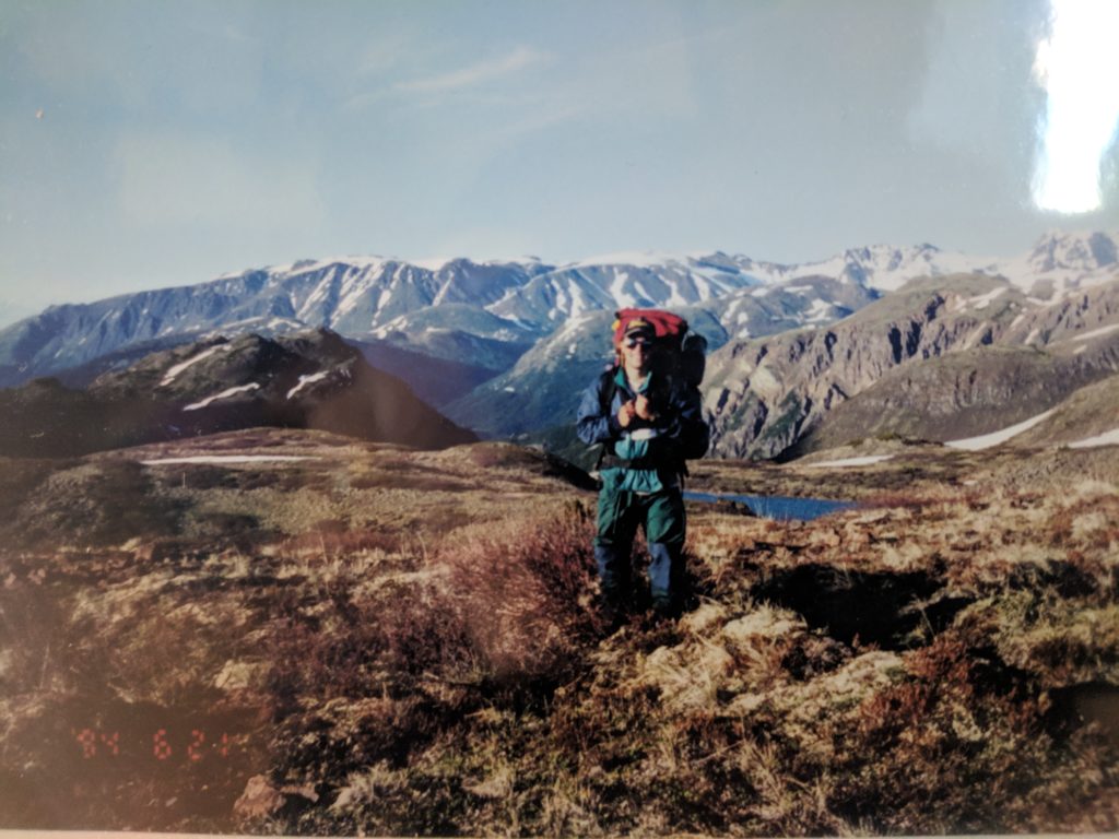Old scanned photograph of Nick standing in the wilderness with backpack on and big mountain views.